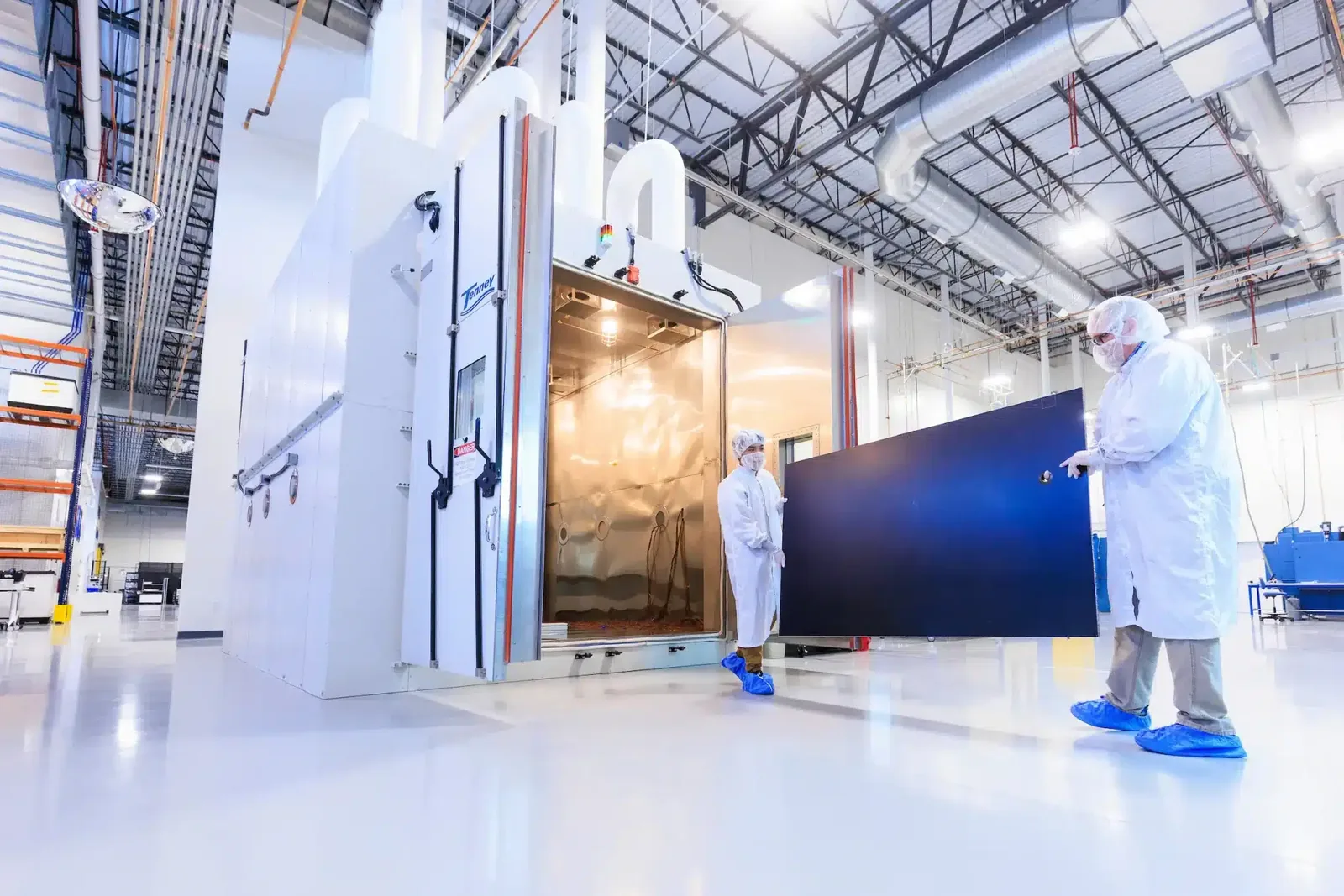 Two Sierra Space technicians testing a solar array beside an environmental chamber